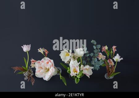 Verschiedene blühende Blüten mit welligen, sanften Blütenblättern, die auf dünnen Blüten wachsen Stiele mit grünen Blättern Stockfoto