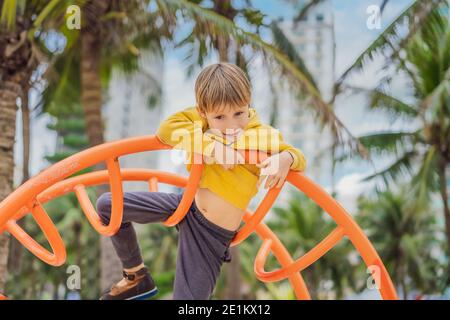 Der Junge klettert auf dem Spielplatz vor dem Hintergrund von Palmen Stockfoto