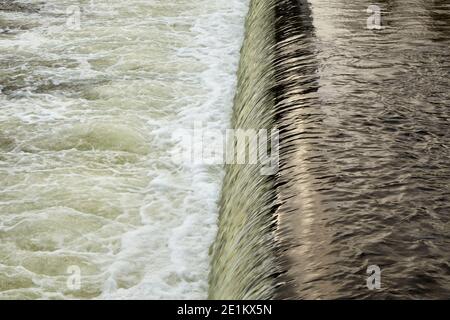 Wasser fällt über ein kleines Wehr, was zu Schaum auf Der Fluss Stockfoto