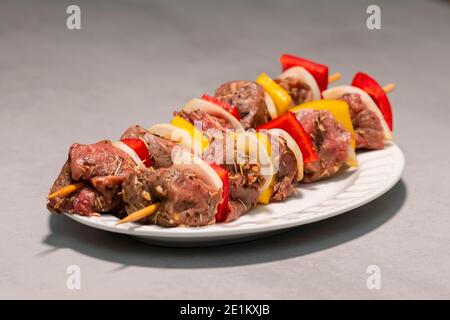 Zwei gewürzte Rinderspieße auf einem weißen Teller, fertig zum Kochen. Selektiver Fokus und Nahaufnahme. Fleisch- und Kochkonzept. Stockfoto