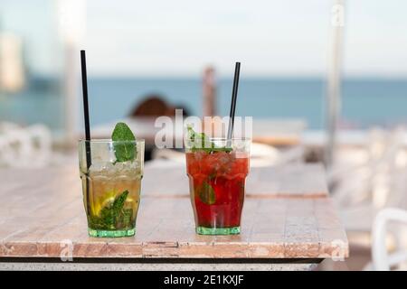 Appetitliche Cocktails mit Strohhalmen auf einem Holztisch auf einem unfokussierten Hintergrund. Selektiver Fokus. Freizeit- und Lifestyle-Konzept. Stockfoto