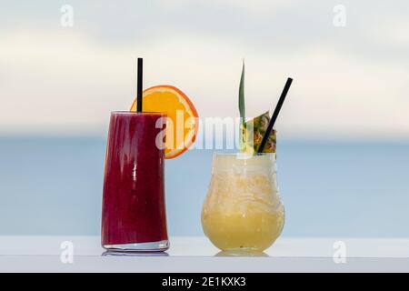 Zwei verschiedene Cocktails mit Fruchtstücken und Strohhalmen an einer Wand auf einem unscharf-hellen Hintergrund. Selektiver Fokus und Nahaufnahme. Freizeitkonzept. Stockfoto