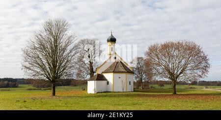 Raisting, Deutschland - 13. Nov 2020: Seitenansicht der Kirche St. Johannes der Täufer. Traditionelle bayerische Kirche steht zwischen t Stockfoto