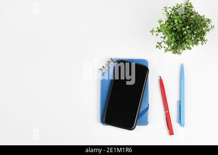 Arbeitstisch mit Smartphone, Notebook, Blume und zwei Stiften. Draufsicht. Flach layierte Kopiefläche Stockfoto