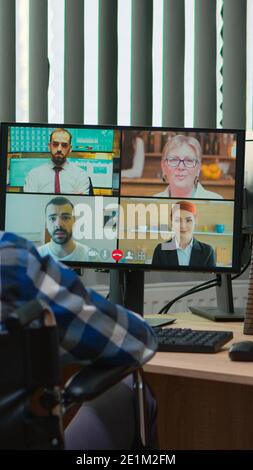 Behinderter Manager im Rollstuhl, der während der Videokonferenz im Geschäftsbüro online spricht. Gelähmt, immobilisiert Freiberufler arbeiten in Finanzunternehmen mit moderner Technologie. Stockfoto