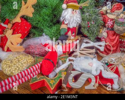 Weihnachtsdekorationen, weiches Spielzeug und Ornamente auf einem Tisch, eine Szene, die verwendet werden könnte, um Dekorationen bereit zum Aufhängen oder zum Ablegen darstellen. Stockfoto