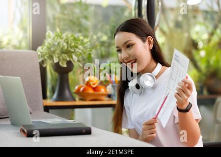 Asiatische Frau Student sitzt am Tisch im Wohnzimmer, hält Kaffeetasse und mit Computer-Laptop, wenn Online-Kurs zu studieren Stockfoto