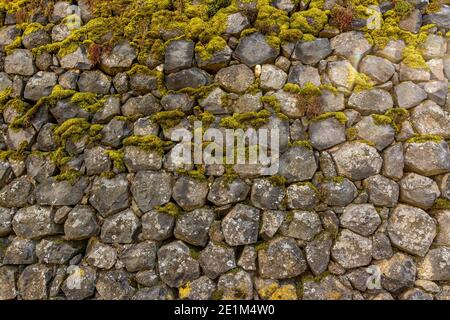 Einzigartige Natursteinmauer, bedeckt mit Moos, in einer ruhigen Umgebung im Freien während der Tageslichtstunden Stockfoto