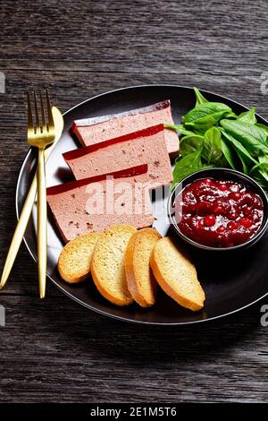 Französisches Gericht Entenleber Pastete mit Cranberry Marmelade auf einem schwarzen Teller serviert mit Cranberry-Sauce, Spinat und Brioche Croutons, mit goldenem c Stockfoto