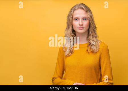 Taille bis Porträt von schönen jungen ernst clever blonde skandinavischen Frau auf hellgelb orange Wand Stockfoto