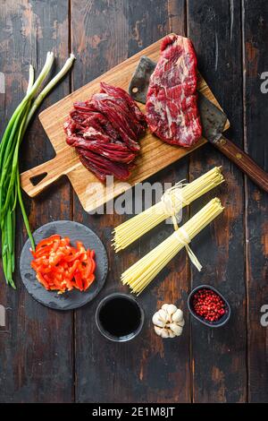 Kochkomponenten für die Herstellung von geschmorten Yakisoba mit Rindfleisch. Flap Steak und Nudeln auf Holzhintergrund Stockfoto