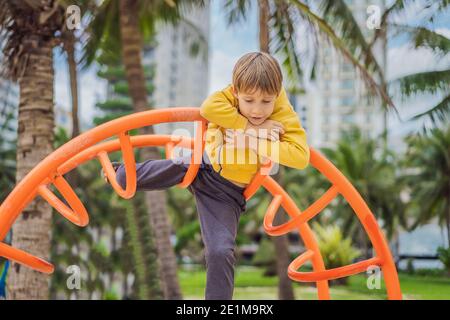Der Junge klettert auf dem Spielplatz vor dem Hintergrund von Palmen Stockfoto