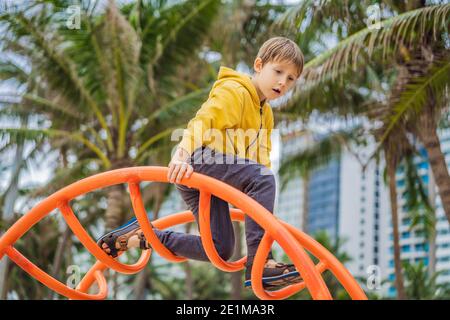 Der Junge klettert auf dem Spielplatz vor dem Hintergrund von Palmen Stockfoto