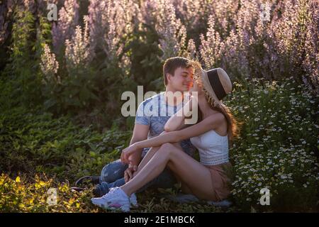 Glückliches Paar in der Liebe sitzt umarmt von einem blühenden Salbei Feld. Ein junger Mann umarmt leidenschaftlich, hält die Hände fest, blickt in die Augen eines schönen Mädchens hinein Stockfoto