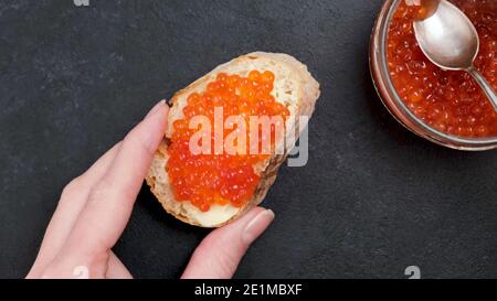 Roter Kaviar und Butter auf Weißbrotscheibe. Frauenhand mit Canape mit rotem Kaviar Stockfoto