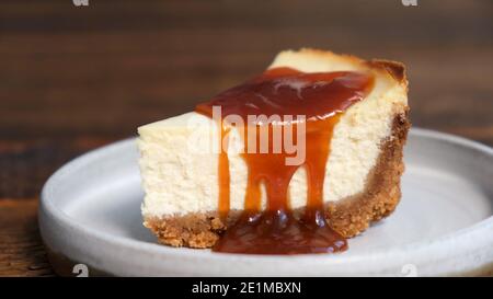 Käsekuchen mit Karamellsauce, Holzhintergrund, Nahaufnahme. Gesalzene Karamellsauce auf Käsekuchen gegossen Stockfoto