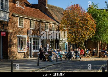 Tische und Stühle außerhalb malerischen Straßencafés, Menschen sitzen in der Herbstsonne, entspannen, Erfrischungen - Scenic College Street, York, England, Großbritannien Stockfoto