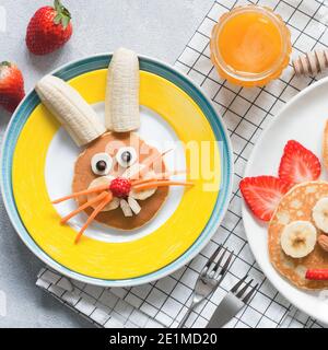 Kreatives Frühstück für Kinder zu Ostern. Hase-förmige süße Pfannkuchen mit Früchten, Beeren und Honig. Babynahrung Stockfoto