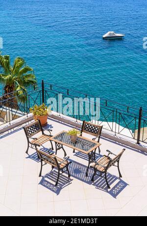 Blick auf die Ägäis über Tisch und Stühlen auf einem Balkon im Ferienort Masouri, Kalymnos, Dodekanes, Griechenland Stockfoto