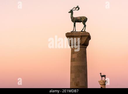 Sonnenuntergang über den bronzenen Hirsch Statuen am Eingang Mandraki Hafen, Rhodos, Insel Rhodos, Griechenland Stockfoto