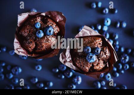 Draufsicht auf köstliche Schokoladen-Cupcakes mit Heidelbeer-Füllung, um die sich reife Beeren von wilden Blaubeeren legen. Süßes Gebäck. Stockfoto