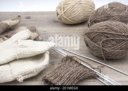 Garnknäuel und gestrickte Fäustlinge auf einem hölzernen Hintergrund. Das Konzept von Hobby, Heimproduktion und individuellem Unternehmertum. Stockfoto