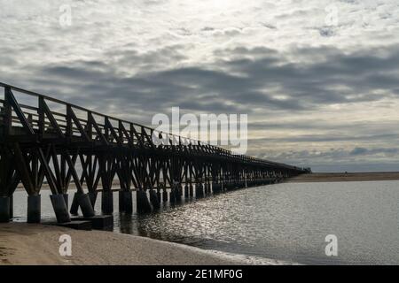 Ein langer hölzerner Steg Pier führt von einem Strand zu Ein weiterer über einem kleinen Meeresarm Stockfoto