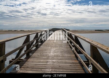 Ein langer hölzerner Steg Pier führt von einem Strand zu Ein weiterer über einem kleinen Meeresarm Stockfoto