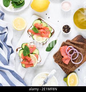 Lachs-Sandwiches mit Frischkäse, Gurken auf weißem Holzbrett, Blick von oben. Flache Lay-Zusammensetzung, quadratische Ernte Stockfoto