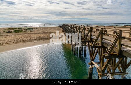 Ein langer hölzerner Steg Pier führt von einem Strand zu Ein weiterer über einem kleinen Meeresarm Stockfoto