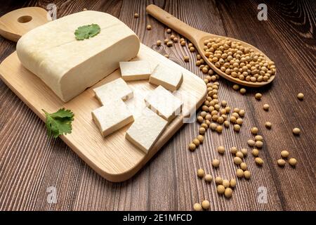 Tofu frisch und Tofu in Scheiben geschnitten auf Holz Schneidebrett mit Sojabohne in Holzlöffel. Volle Tiefe des Feldes. Veganes Food-Konzept. Gesunde Ernährung Stockfoto