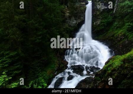 Schöner weicher großer Wasserfall zwischen grünen Pflanzen und Felsen Die Berge Stockfoto