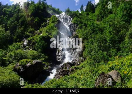 Hoher Wasserfall zwischen Felsen und grünen Sträuchern in den Bergen Bei Sonnenschein Stockfoto