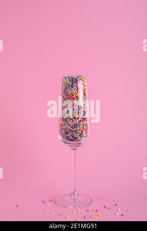 Champagnerglas gefüllt mit bunten Kugeln auf rosa Hintergrund, Party-Konzept Stockfoto