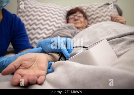 Kranke ältere Frau liegt in einem Bett und liest ein Buch, ältere Frau liest Buch mit Krankenschwester Stockfoto