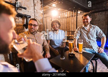 Männer lachen bei Freund, der Wasser trinkt. Bier auf dem Tisch, Pub-Interieur. Stockfoto