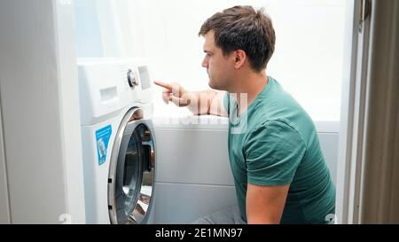 Junger, hübscher Mann, der im Badezimmer eine Waschmaschine gestellt hat. Männlich tun Wäsche und Hausarbeit Stockfoto