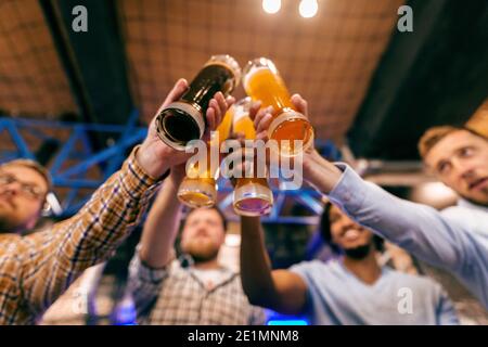 Ansicht von unten von vier männlichen Freunden, die einen Toast mit Bier machen. Pub-Interieur. Stockfoto