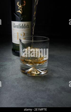 Glenfiddich Single Malt Whisky 12 Jahre alt wird in ein Glas mit Eis auf einer Marmor-Arbeitsplatte gegossen. Stockfoto