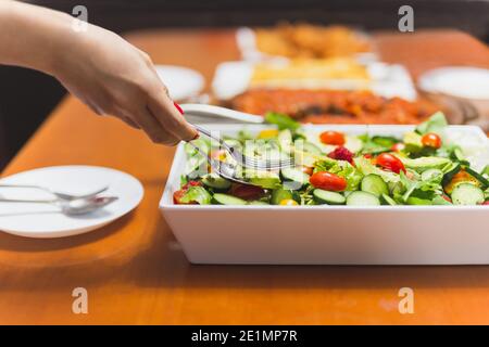 Frau Hände nehmen gemischtes Gemüse in einer Schüssel mit Löffel und Gabel. Stockfoto