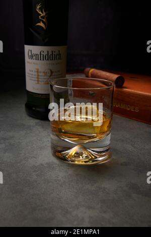 Glenfiddich Single Malt Whisky 12 Jahre alt in einem Glas mit Eis auf einer Marmorarbeitsfläche und einer Schachtel Cohiba Havaan Zigarren im Hintergrund. Stockfoto