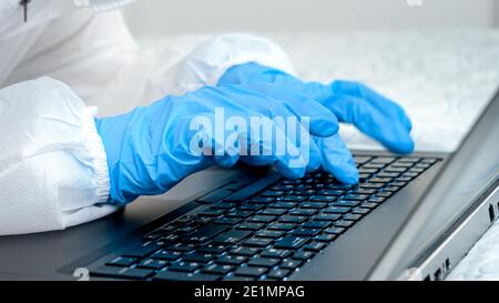 Nahaufnahme des Arztes in medizinischen Schutzhandschuhen, die auf der Laptop-Tastatur tippen. Personen, die sich vor Covid-19 und Coronavirus schützen, während sie aus der Ferne arbeiten Stockfoto