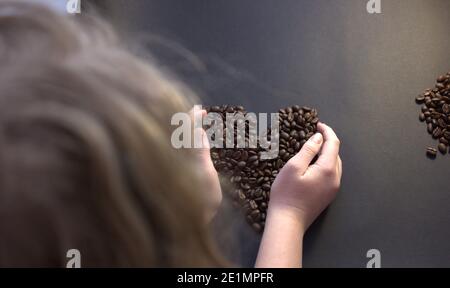 Mädchen macht Herzform von Kaffeebohnen. Draufsicht. Mädchen Hände auf Kaffee. Stockfoto