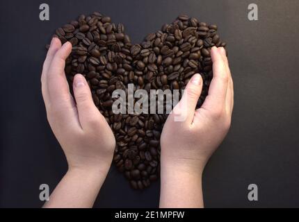 Mädchen macht Herzform von Kaffeebohnen. Draufsicht. Mädchen Hände auf Kaffee. Stockfoto