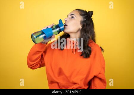 Junge schöne Frau trägt Sweatshirt hält eine Wasserflasche über Isoliertes Trinkwasser mit gelbem Hintergrund Stockfoto