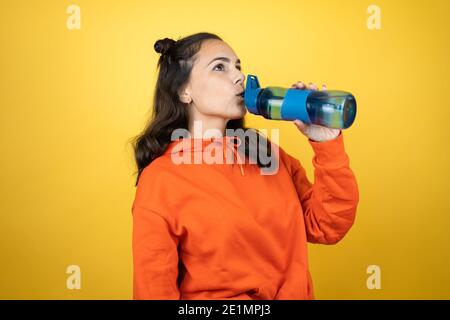 Junge schöne Frau trägt Sweatshirt hält eine Wasserflasche über Isoliertes Trinkwasser mit gelbem Hintergrund Stockfoto