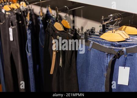 Reihe von aufgehängten blauen und schwarzen Jeans auf hölzernen Kleiderbügel in einem Geschäft. Stockfoto