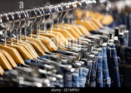 Reihe von aufgehängten blauen und schwarzen Jeans auf hölzernen Kleiderbügel in einem Geschäft. Stockfoto
