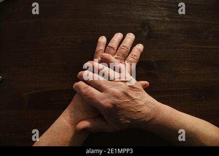 Hände und Arme des alten Mannes, der auf der hölzernen Tischoberfläche liegt. Direkt darüber. Stockfoto