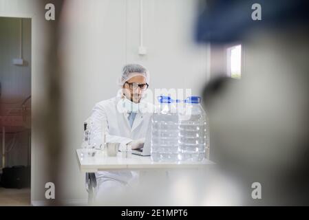 Technologe sitzt auf dem Stuhl und mit Laptop in der Wasserfabrik. Stockfoto